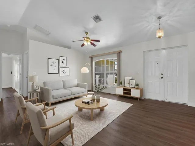 Spacious living area featuring wood-finish flooring, vaulted ceilings, and a ceiling fan with integrated lighting