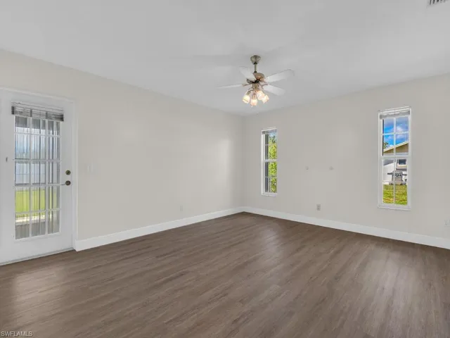 Spacious interior room featuring wood-finish flooring, white baseboards, and a ceiling fan with integrated lighting