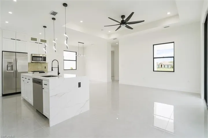Kitchen featuring white cabinetry, appliances with stainless steel finishes, a raised ceiling, light stone countertops, and recessed lighting