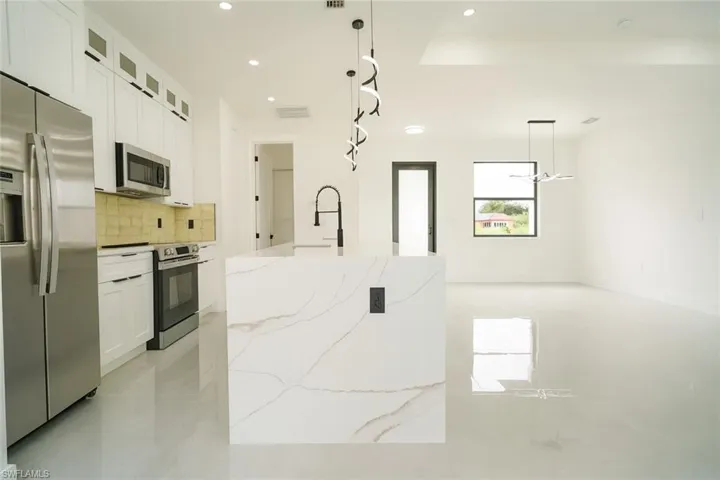 Kitchen with stainless steel appliances, white cabinets, backsplash, light stone counters, and pendant lighting