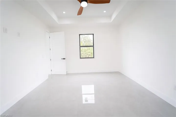 Empty room featuring a raised ceiling, ceiling fan, and light tile patterned flooring