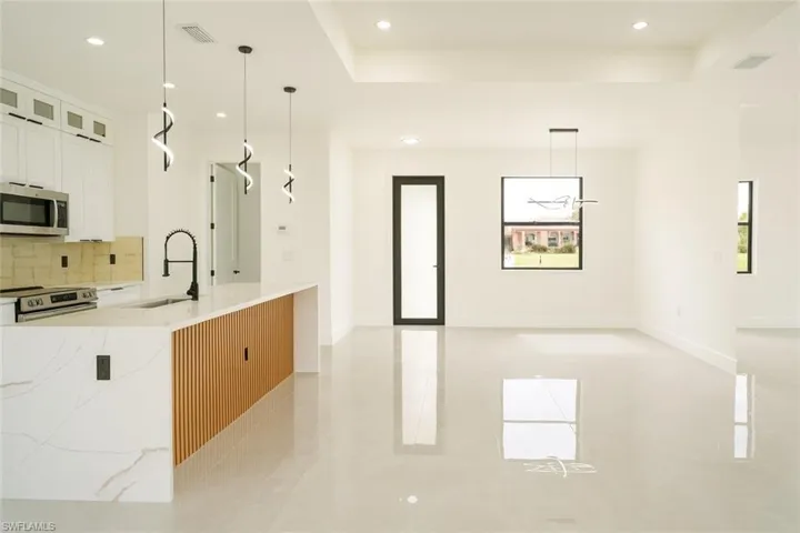 Kitchen with decorative light fixtures, light stone countertops, white cabinets, stainless steel appliances, and recessed lighting