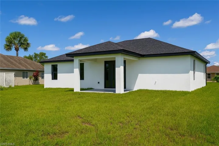 Rear view of house with stucco siding, a lawn, and a patio area
