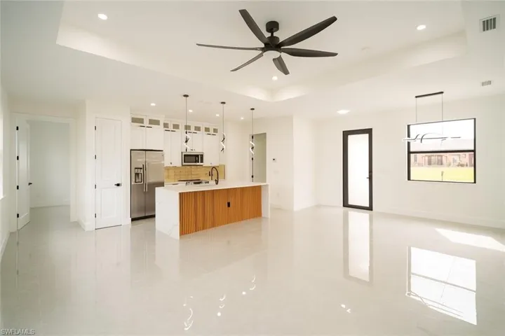 Kitchen featuring glass insert cabinets, a raised ceiling, open floor plan, white cabinets, and decorative backsplash