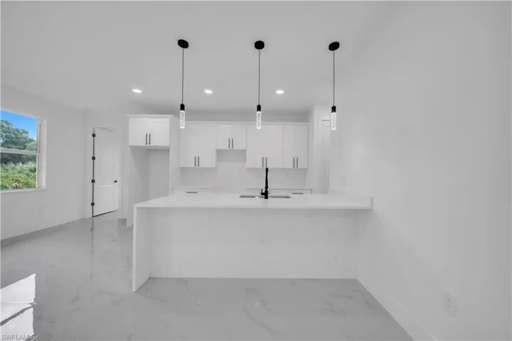 Kitchen featuring a peninsula, light stone counters, white cabinets, hanging light fixtures, and recessed lighting