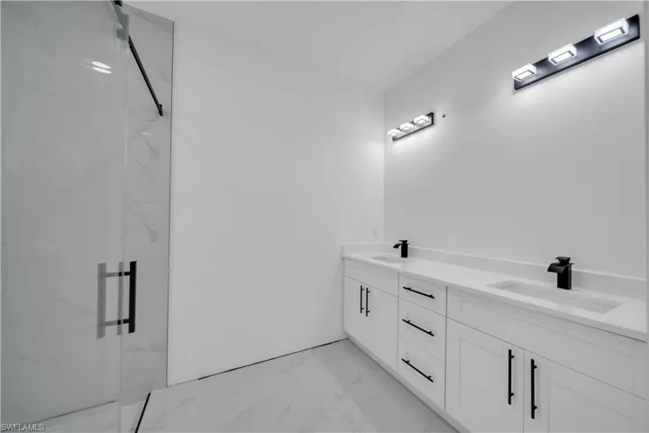 Bathroom featuring light marble finish flooring, double vanity, and a marble finish shower