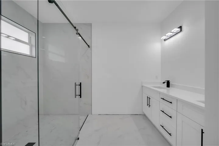 Full bathroom featuring double vanity, a marble finish shower, and light marble finish floors