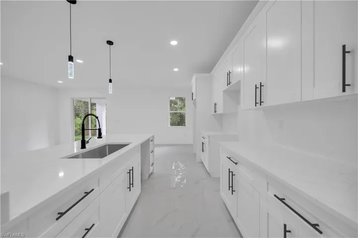 Kitchen featuring white cabinetry, light marble finish floors, recessed lighting, light stone countertops, and decorative light fixtures
