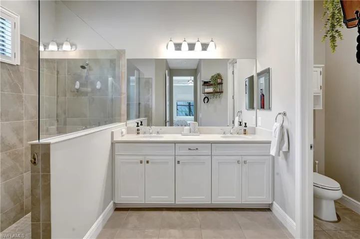 Bathroom featuring double vanity, toilet, a sink, a walk in shower, and tile patterned flooring
