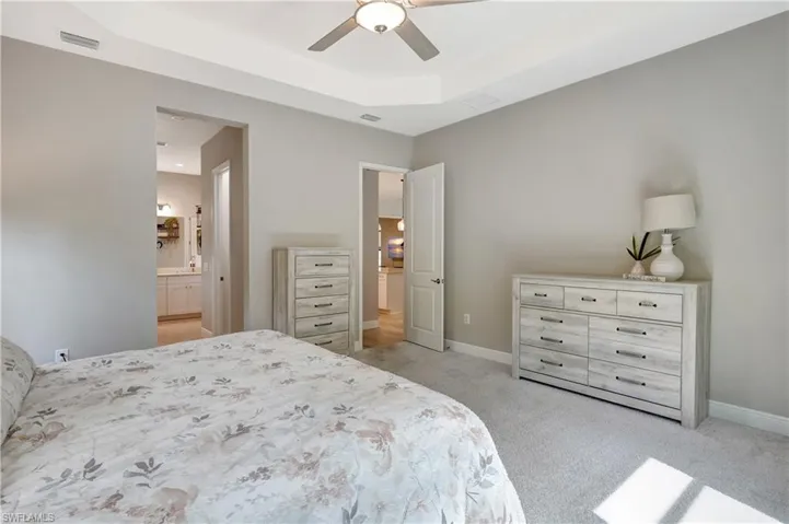 Bedroom with light carpet, baseboards, visible vents, and a raised ceiling