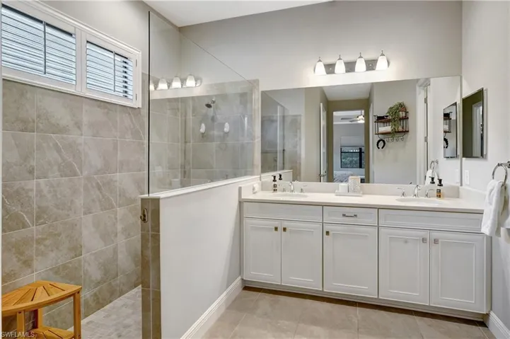 Full bath with double vanity, ceiling fan, a walk in shower, and a sink