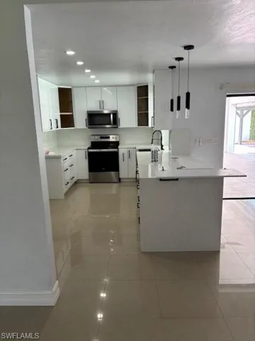 Kitchen featuring stove, white cabinets, decorative light fixtures, a peninsula, and white microwave