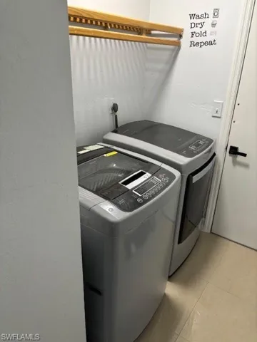 Laundry room with light tile patterned floors, washing machine and dryer, and a textured wall