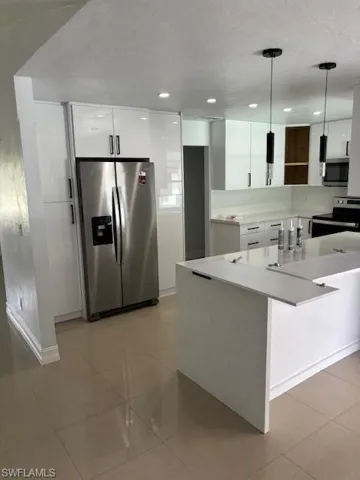 Kitchen with white cabinets, stainless steel fridge, modern cabinets, range, and hanging light fixtures