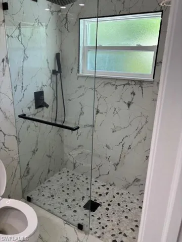 Full bathroom featuring a marble finish shower and toilet