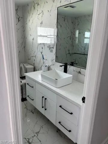 Full bathroom with vanity, light marble finish floors, and tile walls