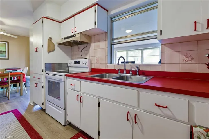 Kitchen with light hardwood / wood-style floors, tasteful backsplash, sink, white range with electric cooktop, and white cabinetry