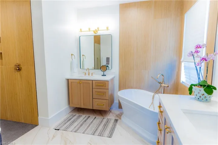 Bathroom featuring vanity, a soaking tub, and light marble finish flooring