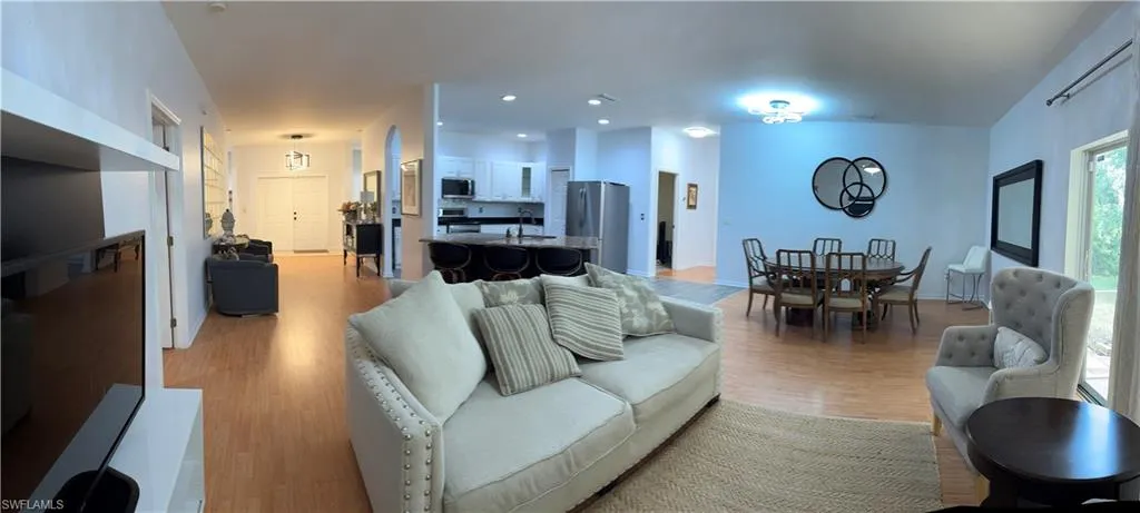 Expansive living area with wood-finish flooring, recessed lighting, arched doorways, and a kitchen featuring white cabinetry and stainless steel appliances