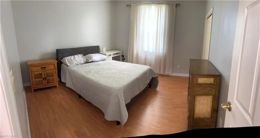 Light gray wall paint, wood-finish flooring, white window treatments, and a white interior door with brass hardware