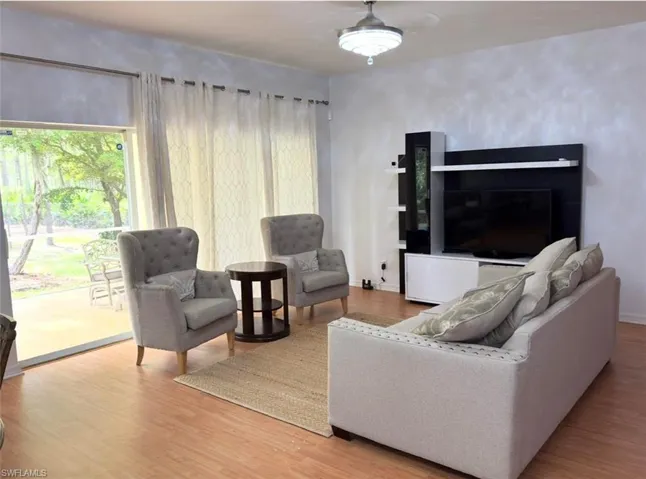 Wood-finish flooring throughout, modern ceiling fan with integrated lighting, built-in entertainment center, and expansive sliding glass doors