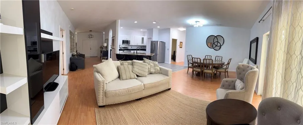 Open-concept living area with wood-finish flooring, a kitchen featuring stainless steel appliances and an island with bar seating, and an adjacent dining area