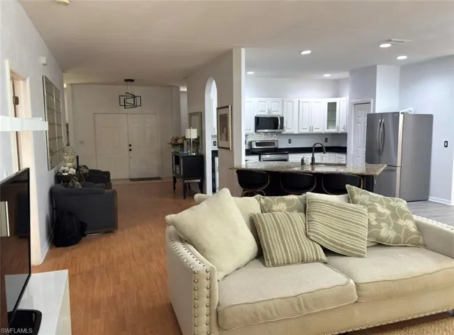 Open-concept living area with wood-finish flooring, recessed lighting, and an arched entryway