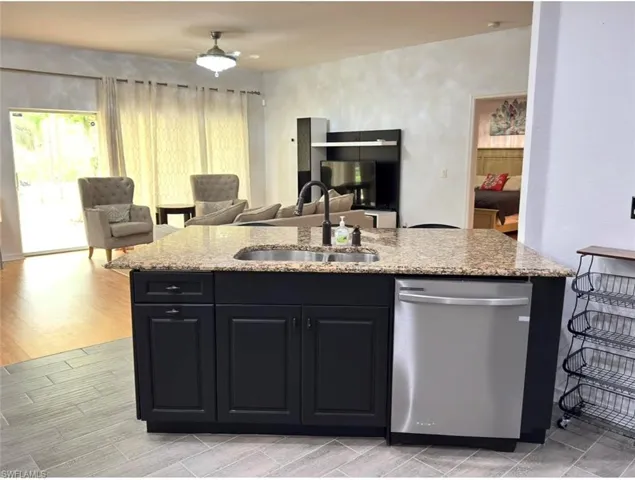 Kitchen island featuring a stainless steel sink, granite-style countertop, and dark cabinetry