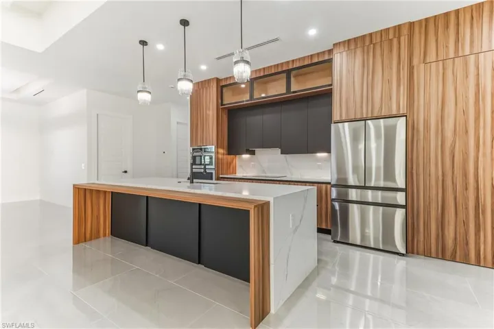 Two tone kitchen featuring dual tone cabinetry, modern cabinets, stainless steel appliances, a center island with sink, and decorative light fixtures