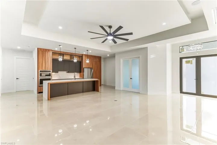 Kitchen with modern cabinets, open floor plan, pendant lighting, center quartz waterfall island with sink and raised ceilings with backlighting.