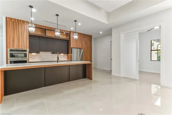 Kitchen with modern cabinets, a large icenter sland with sink, stainless steel appliances, two tone color scheme, and hanging light fixtures
