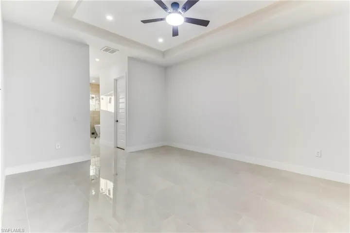 Primary bedroom with a raised ceiling, recessed lighting, and ceiling fan