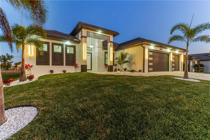 View of front of Modern Luxury pool home with a front yard, Concrete block structure, an attached 3 car garage, and paver driveway