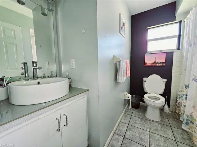 Bathroom with toilet, vanity, baseboards, tile patterned floors, and a shower with curtain