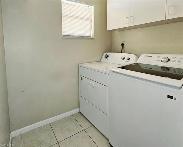 Laundry room with washing machine and dryer, cabinet space, baseboards, and light tile patterned floors