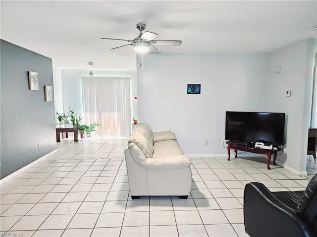 Living area featuring a ceiling fan, light tile patterned floors, and baseboards