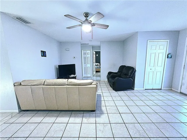 Living area with ceiling fan, baseboards, and light tile patterned floors