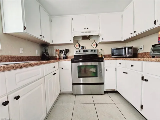 Kitchen featuring stainless steel appliances, under cabinet range hood, light tile patterned floors, and white cabinets
