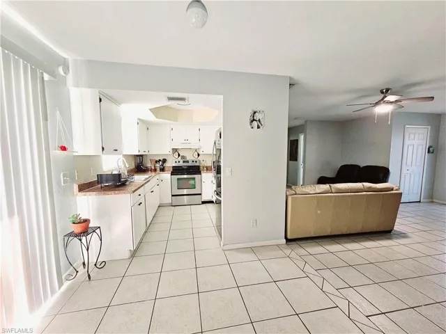 Kitchen with stainless steel appliances, light tile patterned floors, a sink, white cabinetry, and ceiling fan