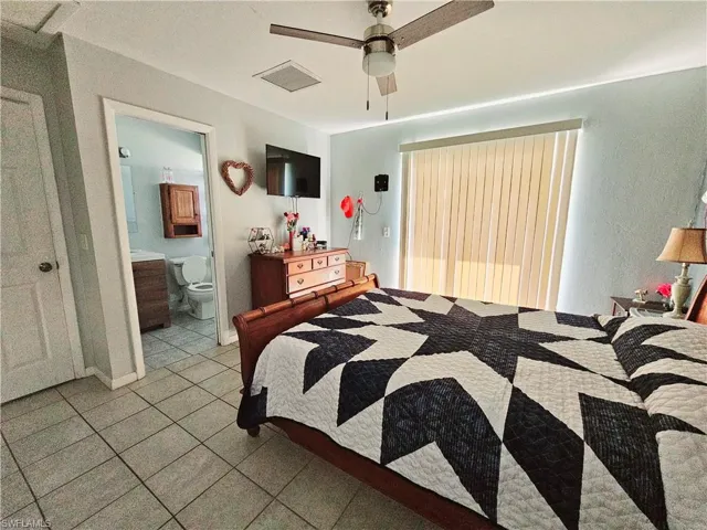 Bedroom featuring light tile patterned floors, connected bathroom, and ceiling fan