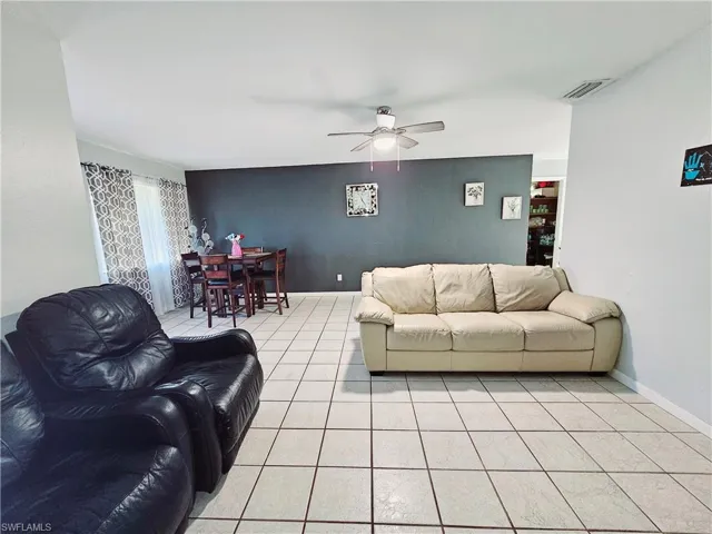 Living room with ceiling fan, an accent wall, light tile patterned floors, and baseboards