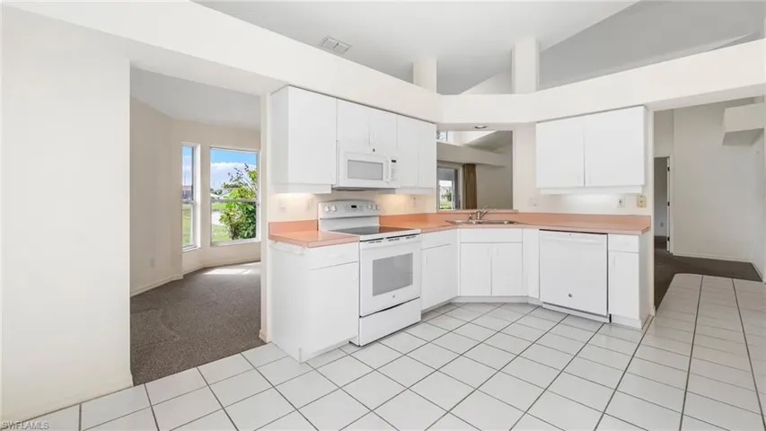 Kitchen with light carpet, white appliances, light countertops, and vaulted ceiling