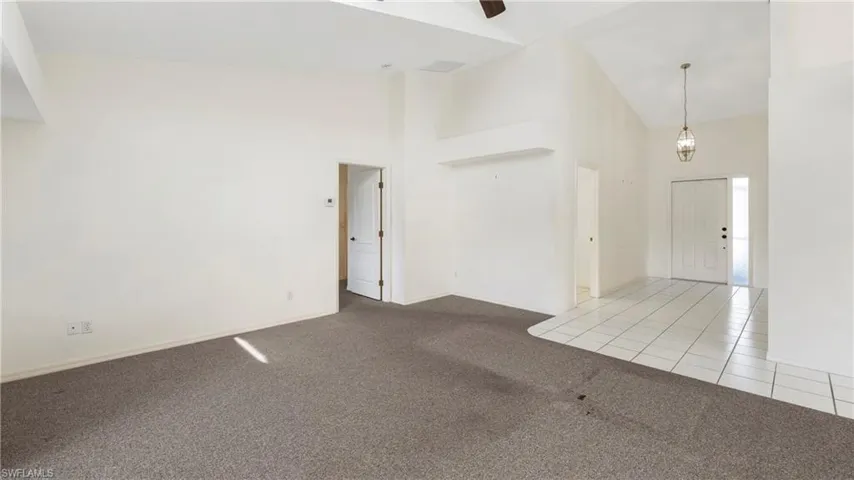 Empty room featuring light colored carpet, vaulted ceiling, ceiling fan, and light tile patterned flooring