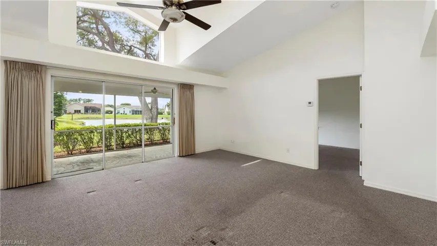Empty room with ceiling fan, dark colored carpet, and lofted ceiling