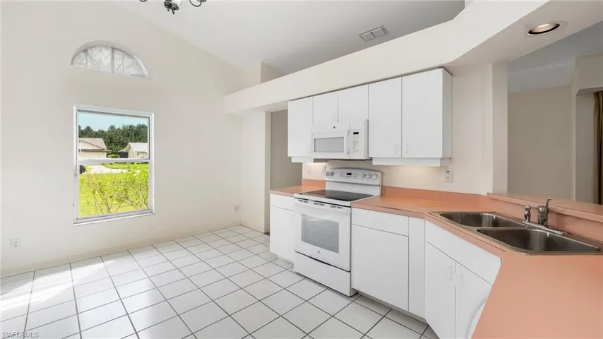 Kitchen featuring white appliances, light countertops, white cabinets, lofted ceiling, and light tile patterned floors