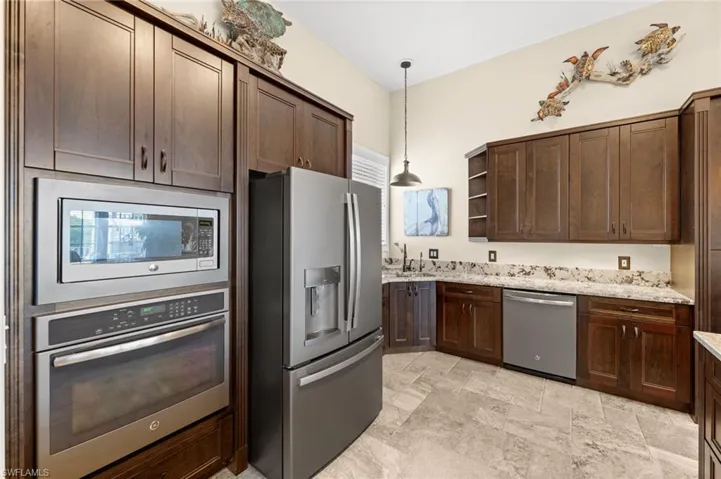 Kitchen featuring appliances with stainless steel finishes, open shelves, dark brown cabinets, pendant lighting, and light stone countertops