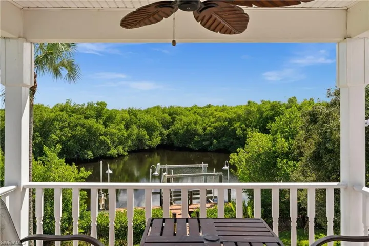 Balcony with boat lift, a water view, a ceiling fan, a boat dock, and view of scattered trees