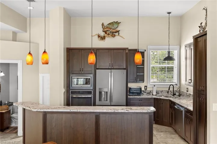 Kitchen with pendant lighting, stainless steel appliances, dark brown cabinets, light stone countertops, and a towering ceiling