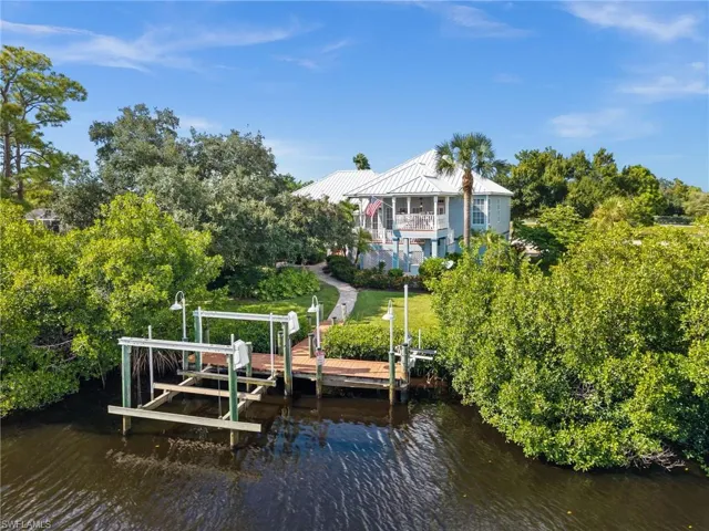 Dock area with boat lift, a water view, a balcony, and a lawn
