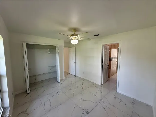 White interior featuring large format marble-look tile flooring, a ceiling fan with integrated lighting, a bifold closet with shelving, and a white interior door
